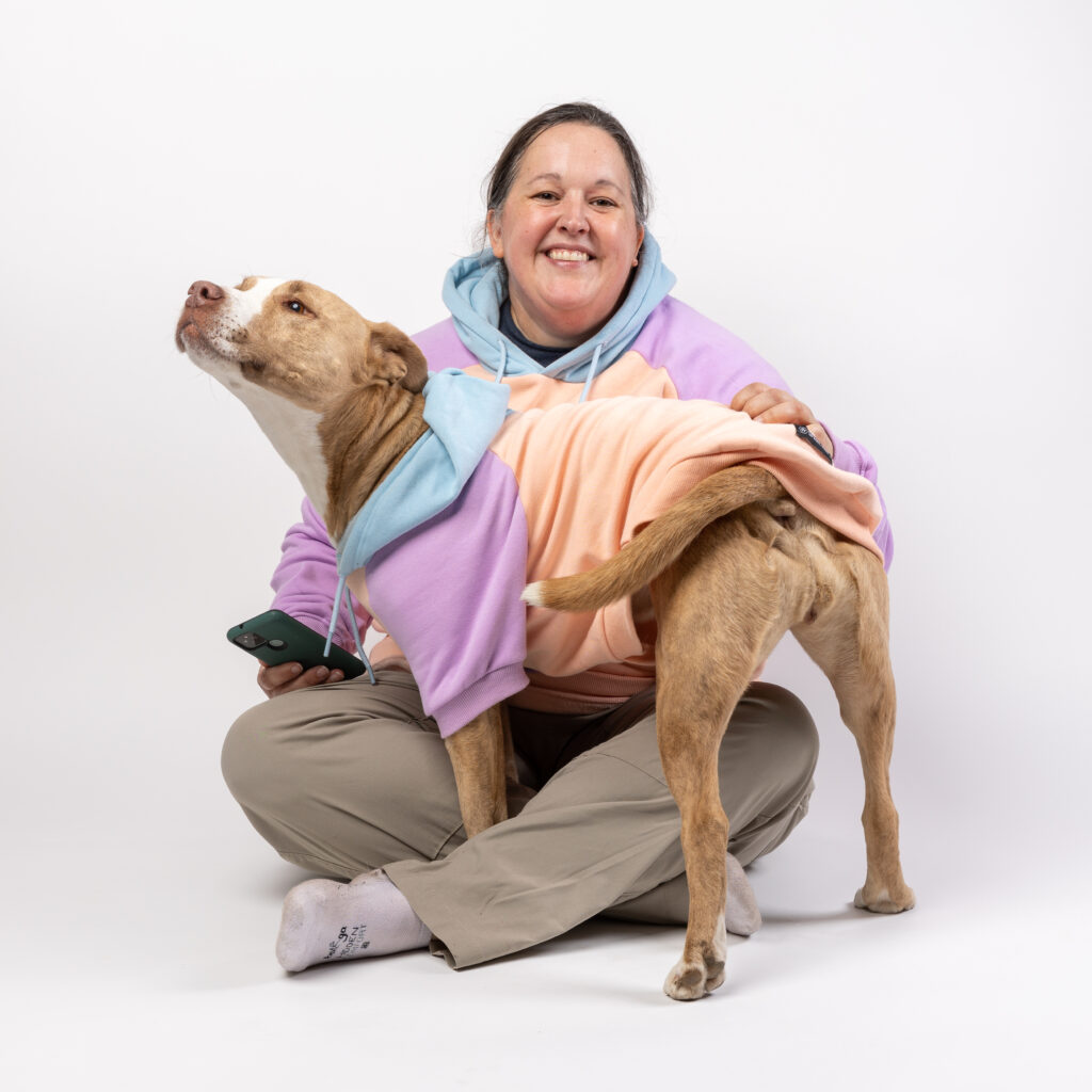 Pet photographer Robyn white is sitting on the ground with her pitbull in her lap. They are wearing matching sweatshirts.