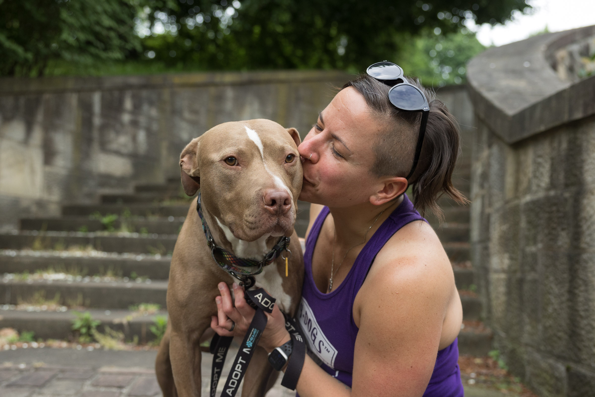 A woman is kissing and snuggling a dog on some concrete steps.