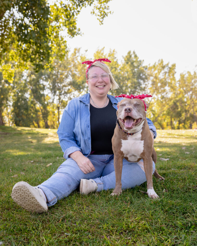 A woman and her senior pitbull are sitting in grass at a park in Cleveland Ohio. Both are smiling and they are wearing matching red polkadot headbands.