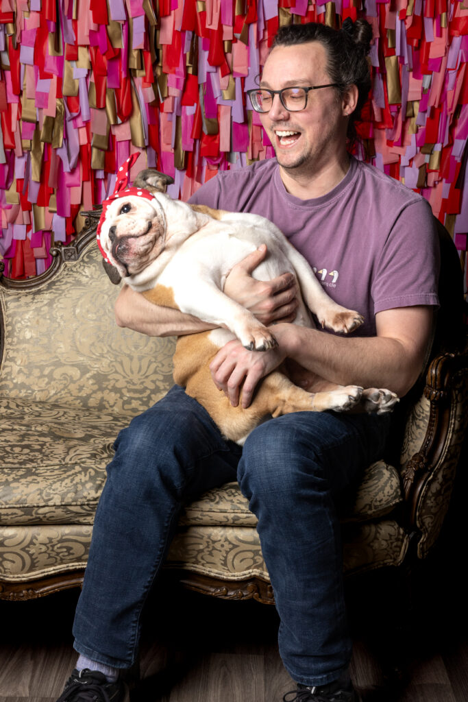 A studio session at Robyn White Photography's studio in Cleveland Ohio features a man smiling at his English bulldog that he's holding in his arms.